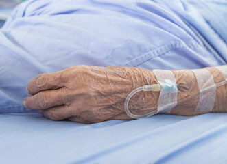 Close up hand of elderly patient with intravenous saline fluid for injection plug in the vein while...