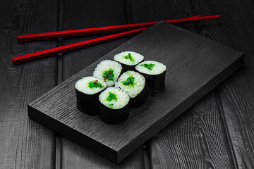 Japanese rolls, maki sushi with chuka seaweed on black wooden background.