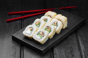 Japanese rolls, sushi with canned tuna, cucumber and cream cheese in sesame on a black wooden background.