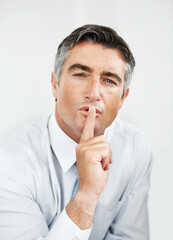 Secret, silent and portrait of businessman in studio for gossip, discretion or confidential company. Professional, quiet and male law attorney with finger on lips for NDA policy by white background.
