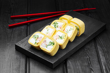 Japanese rolls, sushi in tortilla with shrimp, cucumber and cream cheese on black wooden background.