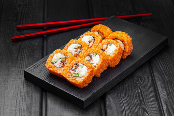 Japanese rolls, sushi made of rice in red sauce with eel, cucumber and cheese on a black wooden background.