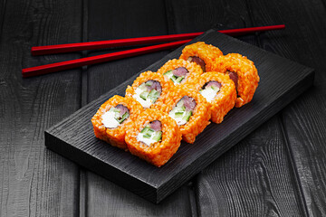 Japanese rolls, sushi made of rice in red sauce with fresh tuna, cucumber and cheese on a black wooden background.