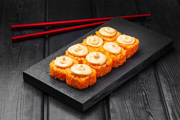 Japanese rolls, rice sushi with cheese sauce on top on black wooden background.
