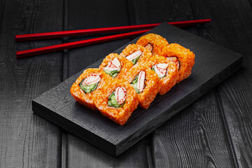Japanese rolls, sushi made of rice in red sauce with crab meat, cucumber and cheese on a black wooden background.