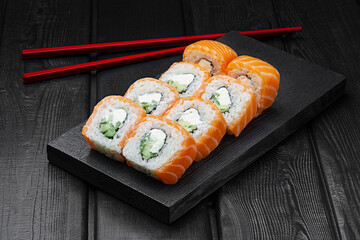 Japanese rolls, Philadelphia sushi with salmon, cucumber and cheese on a black wooden background.