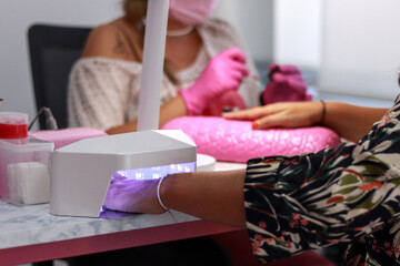 Manicure session with a client's nails under a UV lamp in a salon, manicurist in the background