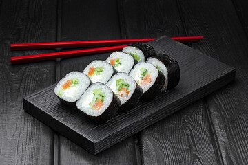 Japanese rolls, sushi with salmon, cucumber and cheese on a black wooden background.