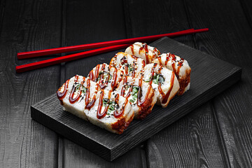 Japanese rolls, rice sushi with eel, teriyaki sauce, cucumber and cheese on a black wooden background.