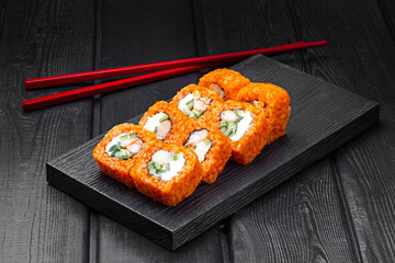 Japanese rolls, sushi made of rice in red sauce with shrimp, cucumber and cheese on a black wooden background.