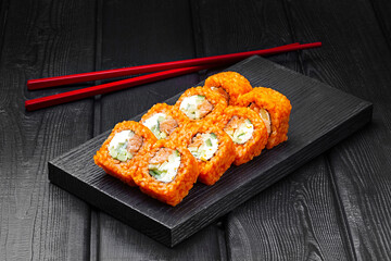 Japanese rolls, sushi made of rice in red sauce with salmon, cucumber and cheese on a black wooden background.