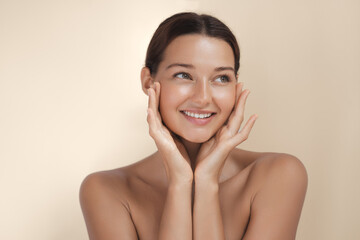 Smiling young woman with glowing skin gently touching her face, captured in soft, natural light....