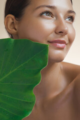 A radiant young woman poses with a large green leaf, emphasizing natural beauty and eco-conscious skincare. Ideal for promoting organic skincare, wellness, and beauty products that embrace nature's