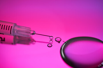 Injection syringe with a drop of drug on a rich pink background.