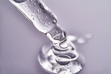 Pipette with facial serum pouring out of it on purple background.