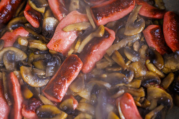closeup view of roasting cut champignon mushrooms and sausages.