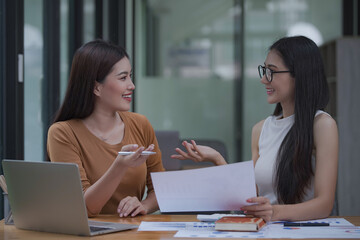 Two young Asian businesswomen discussed investment project work and planning strategy. Business people talk together on laptop computers at the office.