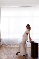 Beautiful slender pregnant girl with makeup and styling in the apartment. A woman waiting for a...