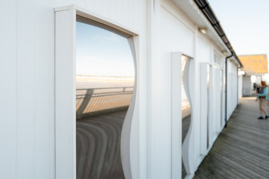 Series of funhouse distorting mirrors seen on a pier at a popular holiday destination on the east coast of Britain. A member of the public is seen looking at a mirror.
