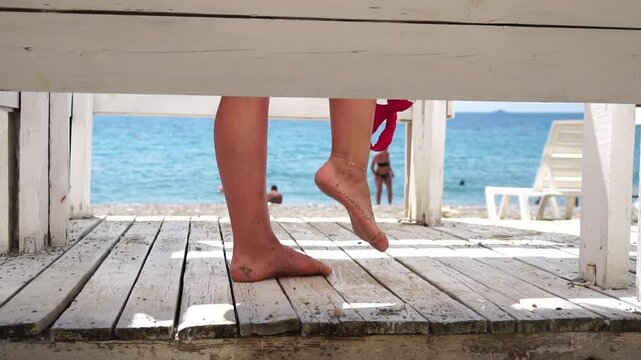 Woman in the changing, dressing room on beach, at sunset on the seashore. Close-up of bare female feet legs in enclosed changing room cabin. Summer holiday vacation and travel concept. Slow motion