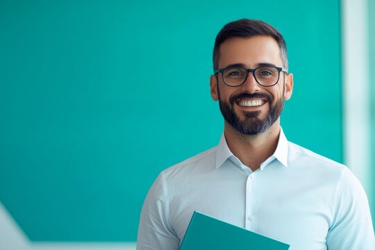 A smiling man with glasses holds a document against a vibrant teal background, exuding professionalism and confidence.