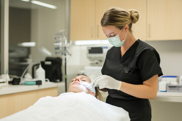 Obraz premium A woman in a black scrub suit is performing a facial on a woman