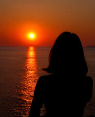 a woman watching a sunset at the sea