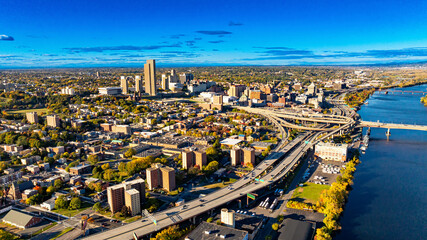 Obraz premium Aerial view of Albany during a clear sunny day. The skyline of Albany showcases vibrant city life with buildings, roads, and a serene river under a bright blue sky.