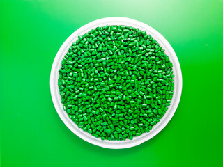 Green masterbatch granules in a cup, isolated on green background, color pigment carrier polymer in...