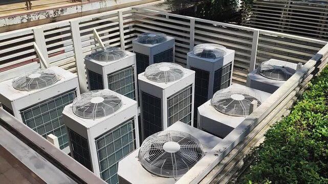 A row of industrial air conditioning units housed in a fenced outdoor enclosure, with large fan vents visible on top, providing cooling for the building.