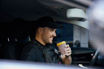 Portrait of smiling patrolman driving car drinking takeaway coffee