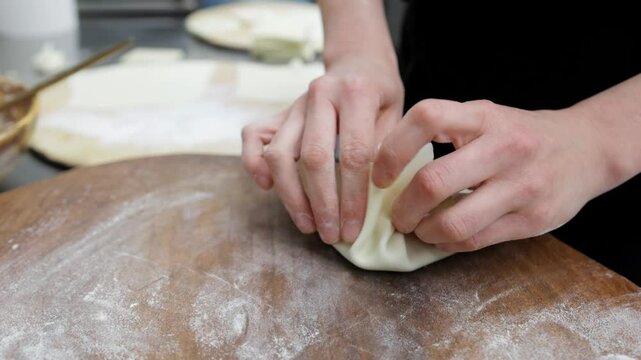 A chef in a restaurant kitchen prepares khinkali, laying out minced meat on dough and wrapping it to mold the desired shape. Ideal for scenes showcasing traditional Georgian cuisine.