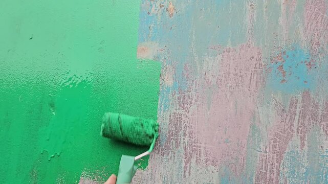 Hand holding a roller and painting a metal surface rusty wall green. Painting matal, repair process