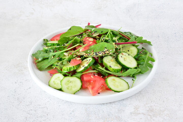 a plate of salad with cucumber, tomato and greens and seeds 