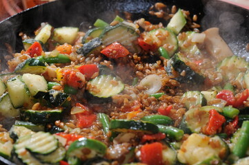 Colorful wok food close-up with steam. zucchini, haricot beans, tomato, onion, grains, mushroom