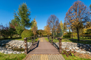 A park with a beautiful landscape design on a sunny day. A small wooden bridge over the .stream.