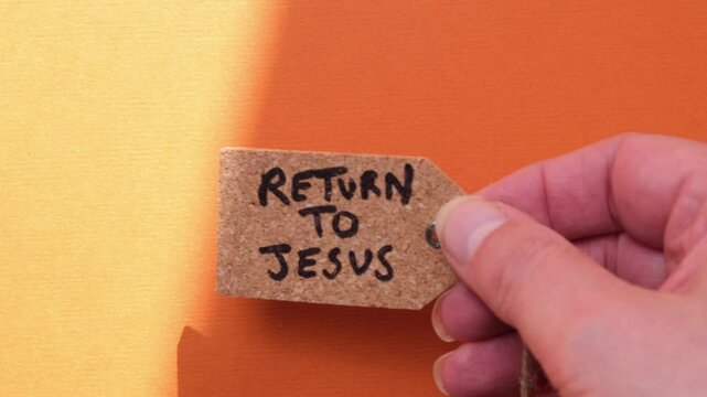 Christianity concept. A person is placing a luggage tag onto a yellow and orange background. On the tag is written Return to Jesus. Concept, evangelism, salvation, Jesus.
