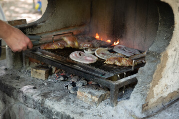 Open flame barbacue with chicken breasts and pork bacon on the mixed grill in a summer day