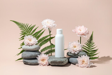 A cosmetics container on a stone podium surrounded by fern leaves, chrysanthemum flowers. A mock-up...
