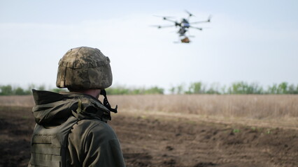 A soldier in camouflage observes a drone hovering above an open field. The drone represents modern...