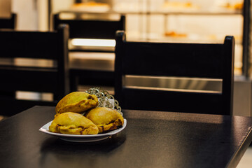 empanadas de harina rellenas de carne, en plato blanco cuadrado, sobre una mesa oscura, en una...