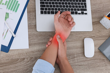 Man suffering from pain in wrist at wooden table, top view. Office work, Carpal tunnel syndrome