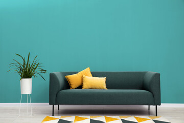 Fototapeta premium Stylish room with comfortable sofa and houseplant near turquoise color wall. Interior design