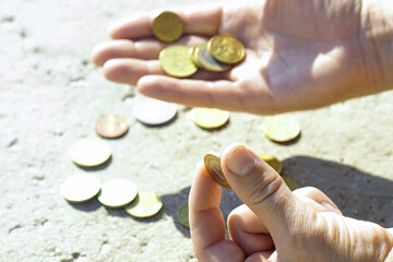 Male fingers holding 1 (one) euro against the background of a hand with coins and small change scattered on the surface, close-up. Saving in the countries of the European Union. Poverty in Europe
