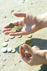 A man collects small coins scattered on the ground. Close-up of male hands holding 1 (one) euro, 50 (fifty), 20 (twenty) and 10 (ten) cent coins. The official money of the Eurozone countries.