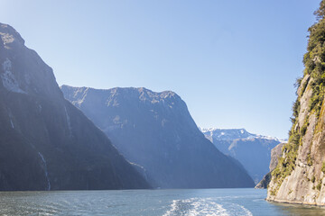 Boat sailing in milford sound fjord with mountains and sun