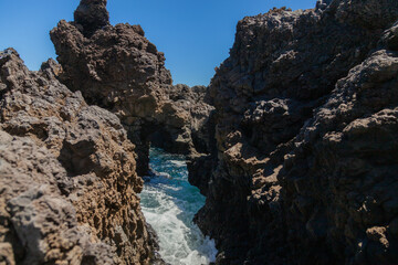 Ocean water flowing between volcanic rocks on sunny day