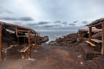 Deserted beach bar showing volcanic lava rock and ocean inlet on overcast day