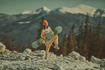  A girl with a snowboard in her hands against the backdrop of snowy mountains