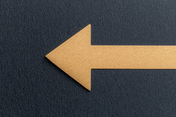 Obraz premium A golden arrow shape pointing left on a textured dark surface, suggesting direction or navigation.